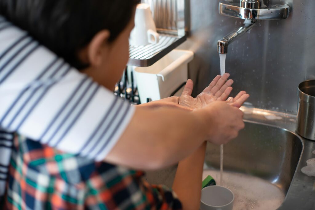 A child practicing hygiene by learning to wash hands under adult supervision at a kitchen sink.